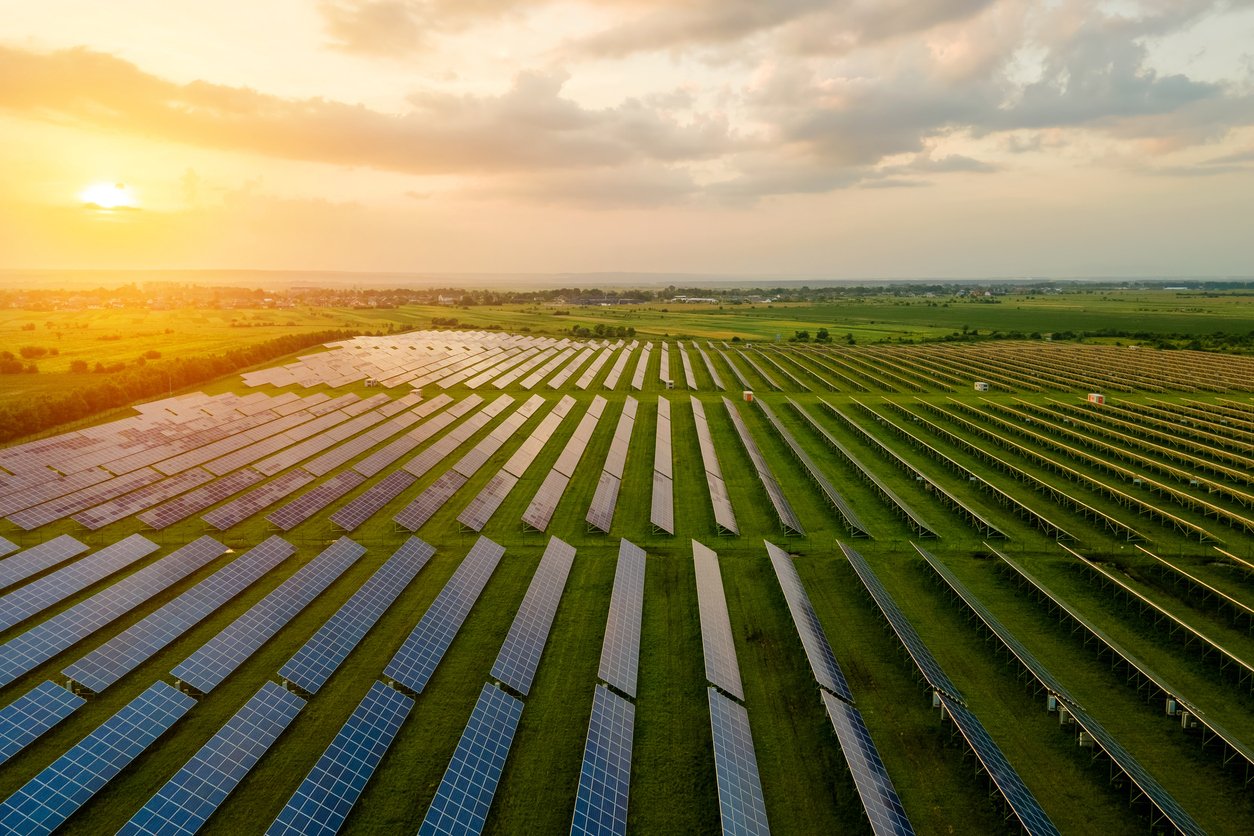 Aerial view of a solar farm with rows of solar panels generating renewable energy at sunset.