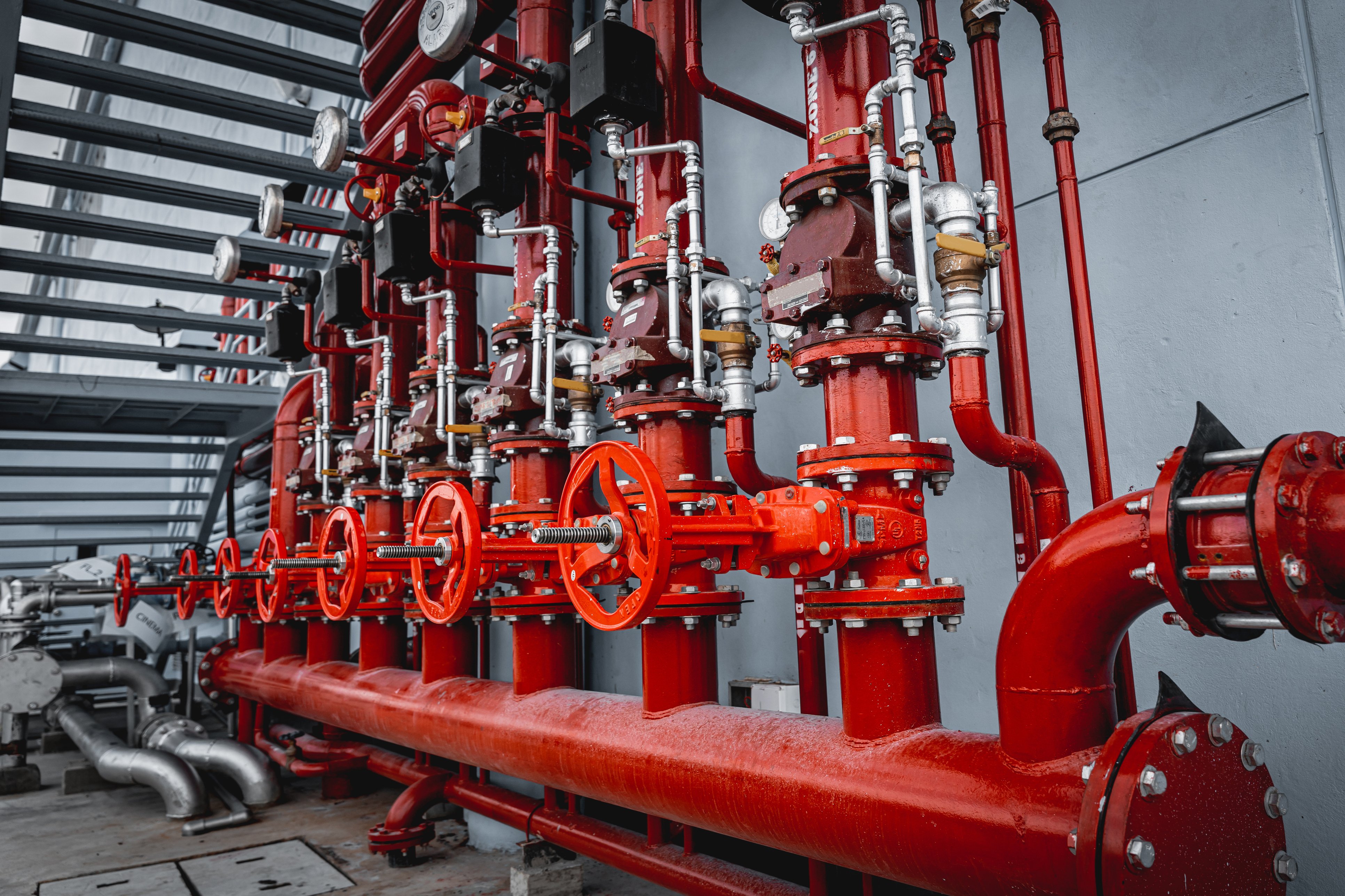 Close-up view of an industrial piping system with multiple red valves, flanges, and connected metal pipes in a facility, showcasing durable infrastructure components.