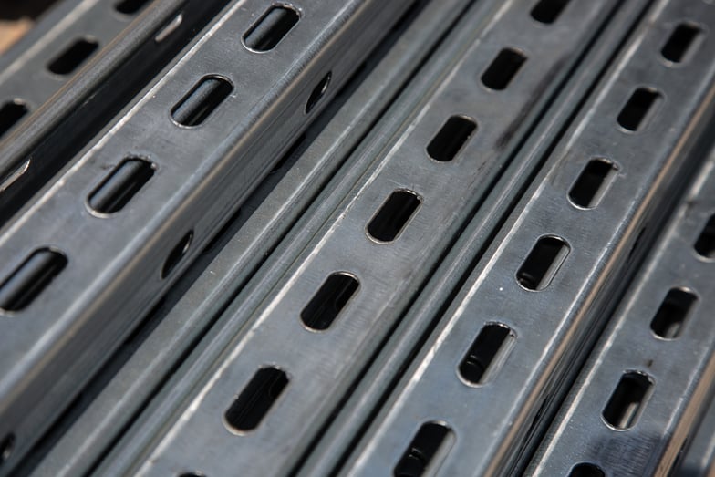 Close-up of galvanized strut channel stacked together, showing slotted openings and industrial steel construction.