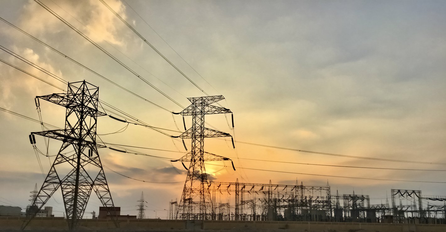 High-voltage power lines and transmission towers at an electrical substation during sunset, representing utility infrastructure and energy distribution.